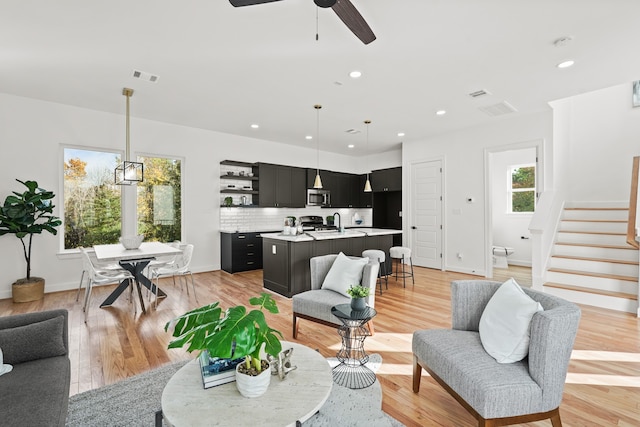 living room featuring ceiling fan with notable chandelier and light wood-type flooring