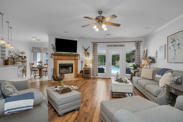 living room featuring light hardwood / wood-style flooring, ceiling fan, a fireplace, and crown molding