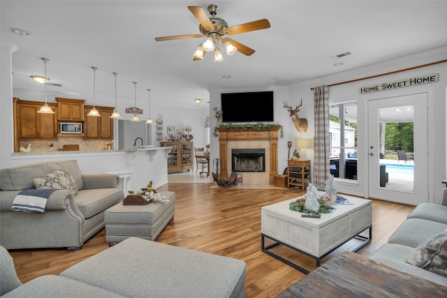 living room with a tiled fireplace, ceiling fan, sink, light hardwood / wood-style flooring, and ornamental molding