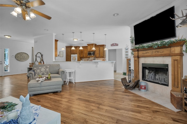 living room with a tiled fireplace, ceiling fan, crown molding, and light wood-type flooring