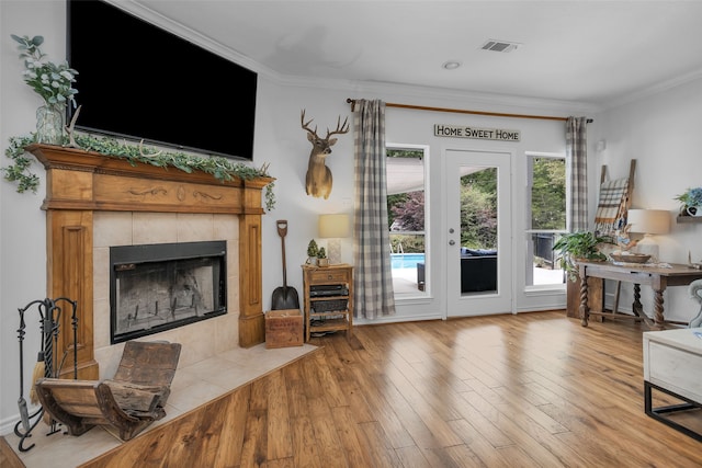 living room with light hardwood / wood-style floors, a tile fireplace, and ornamental molding