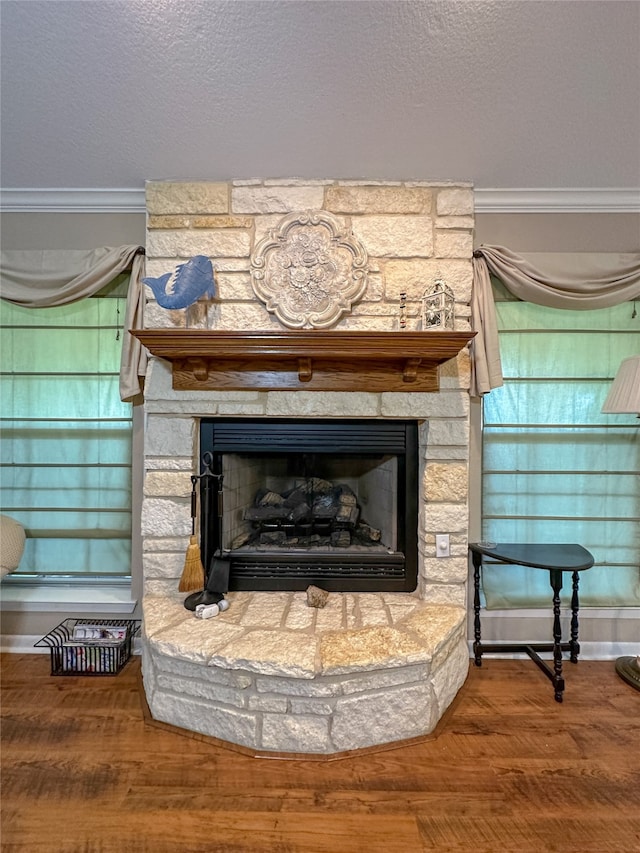 interior details featuring ornamental molding, a stone fireplace, dark hardwood / wood-style floors, and a textured ceiling