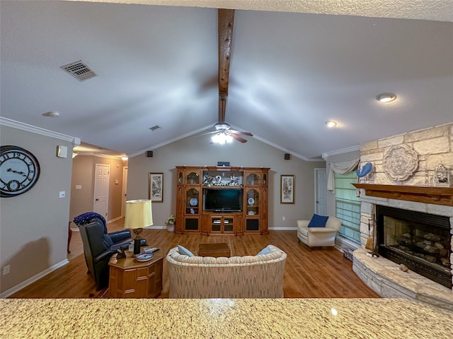 living room featuring dark wood-type flooring, ceiling fan, a stone fireplace, lofted ceiling with beams, and ornamental molding