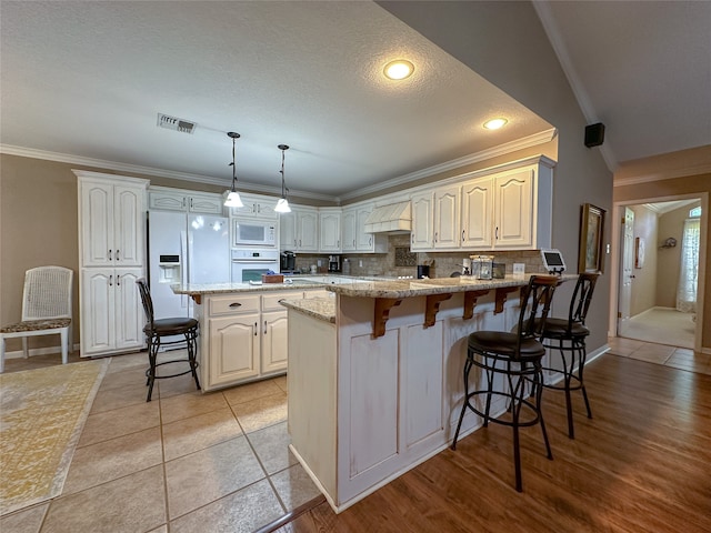 kitchen featuring light stone countertops, white appliances, a kitchen breakfast bar, light hardwood / wood-style floors, and ornamental molding