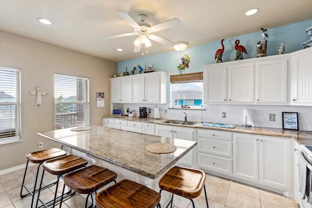 kitchen with ceiling fan, a breakfast bar area, backsplash, light stone countertops, and white cabinets