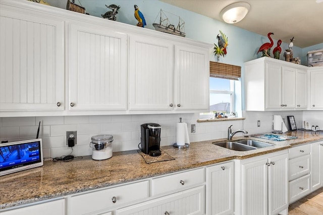 kitchen with tasteful backsplash, white cabinets, sink, and light stone countertops