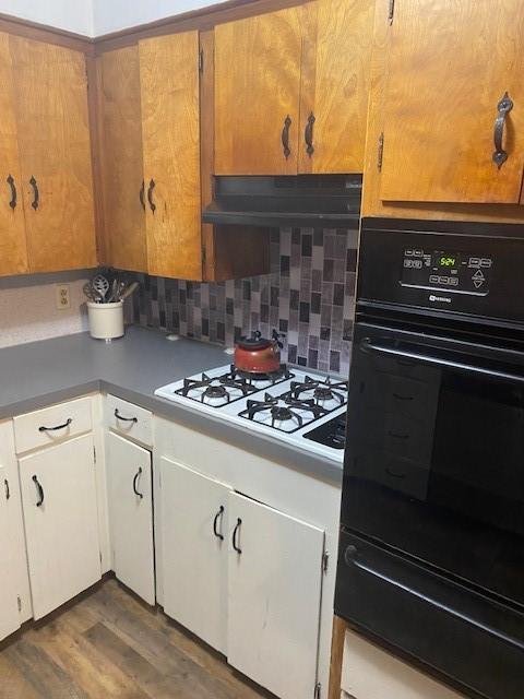 kitchen with backsplash, extractor fan, white cabinetry, hardwood / wood-style floors, and black oven