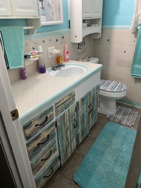 bathroom featuring vanity, toilet, and tile walls