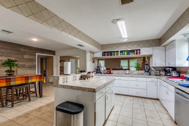 kitchen featuring dishwasher, white cabinetry, light tile flooring, and a kitchen island