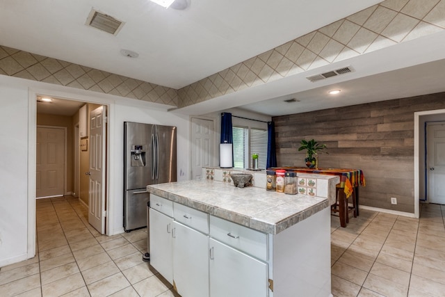 kitchen featuring white cabinetry, a kitchen island, light tile floors, wooden walls, and stainless steel fridge with ice dispenser