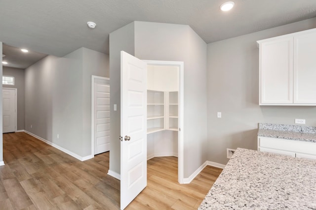 interior space featuring light hardwood / wood-style floors, light stone counters, and white cabinets