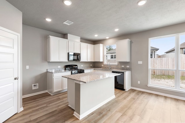 kitchen with black appliances, white cabinetry, a kitchen island, and light hardwood / wood-style floors