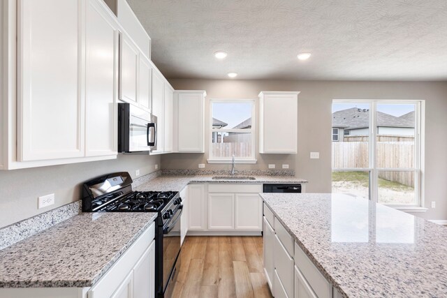 kitchen featuring black gas stove, a healthy amount of sunlight, sink, and light wood-type flooring