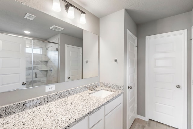 bathroom with vanity, an enclosed shower, a textured ceiling, and hardwood / wood-style flooring