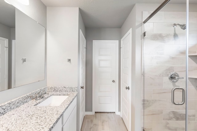 bathroom featuring vanity, a textured ceiling, a shower with shower door, and hardwood / wood-style floors