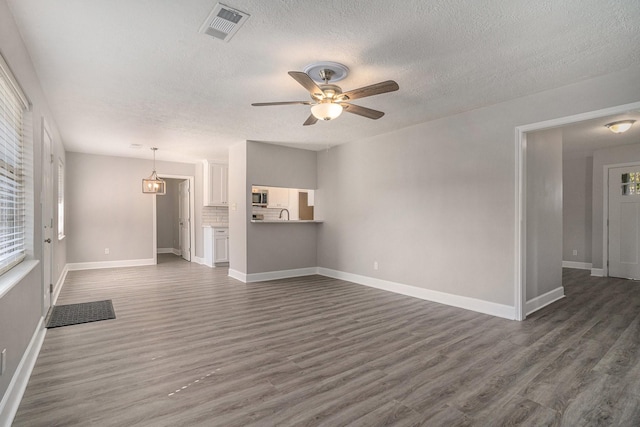 unfurnished living room with a textured ceiling, dark hardwood / wood-style flooring, and ceiling fan