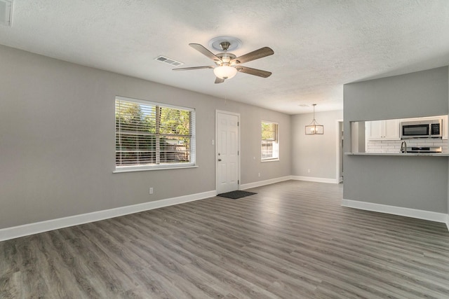 unfurnished living room featuring ceiling fan, dark hardwood / wood-style flooring, and a textured ceiling