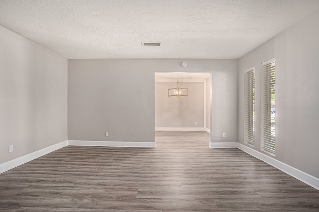 unfurnished room with a textured ceiling, dark hardwood / wood-style floors, and an inviting chandelier