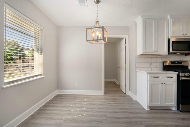 kitchen with backsplash, an inviting chandelier, white cabinets, appliances with stainless steel finishes, and decorative light fixtures