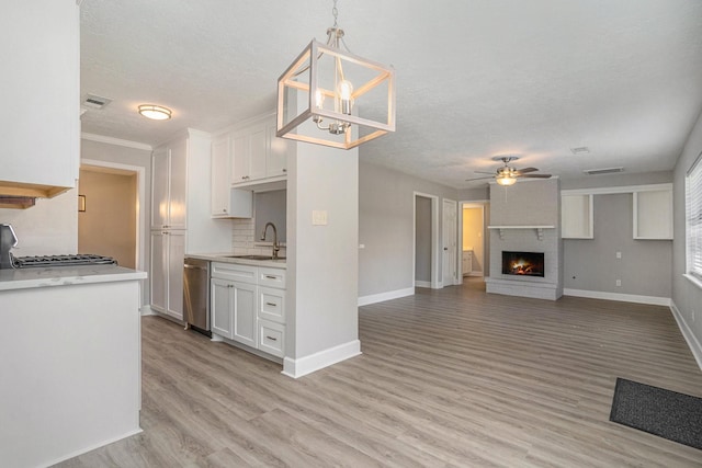 kitchen with pendant lighting, white cabinets, ceiling fan with notable chandelier, sink, and stainless steel dishwasher