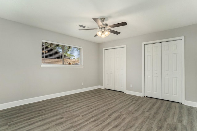 unfurnished bedroom featuring dark wood-type flooring, ceiling fan, and multiple closets