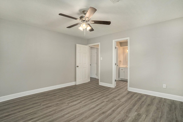 unfurnished bedroom with ensuite bathroom, ceiling fan, and dark wood-type flooring