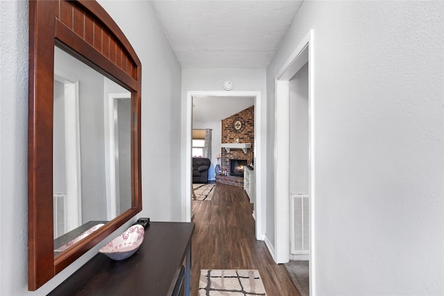 hall featuring brick wall, dark wood-type flooring, and a textured ceiling