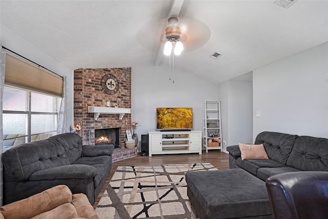 living room featuring ceiling fan, a fireplace, dark hardwood / wood-style flooring, brick wall, and lofted ceiling with beams