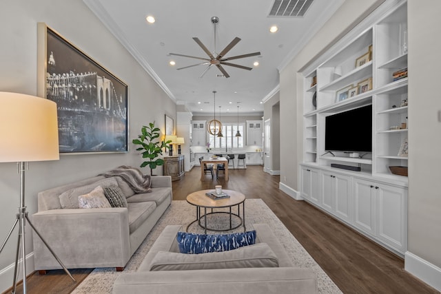 living room featuring built in shelves, ceiling fan, ornamental molding, and dark hardwood / wood-style floors