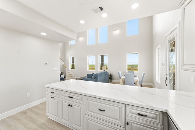 kitchen featuring light stone countertops, light wood-type flooring, white cabinetry, and a towering ceiling