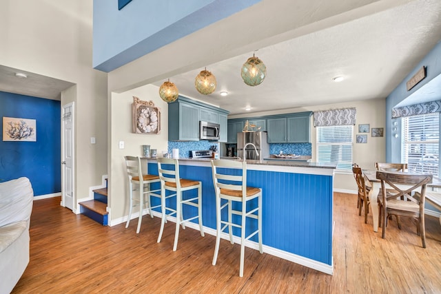 kitchen with blue cabinetry, light hardwood / wood-style floors, kitchen peninsula, a breakfast bar area, and appliances with stainless steel finishes