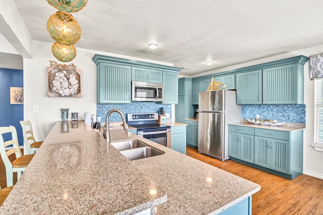 kitchen featuring light stone counters, stainless steel appliances, a kitchen bar, decorative light fixtures, and light hardwood / wood-style flooring