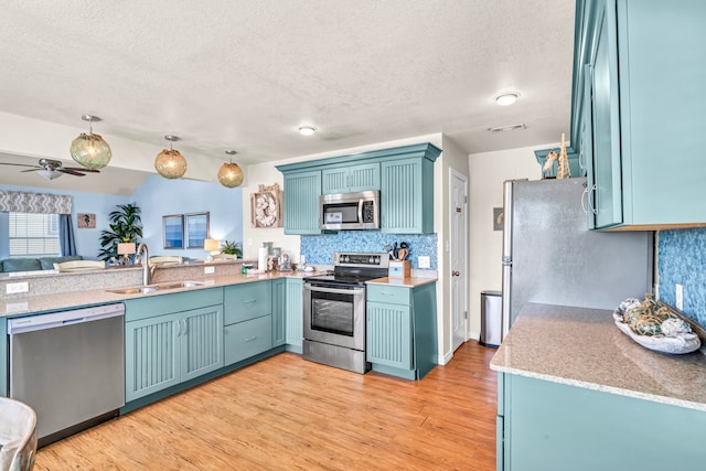 kitchen with decorative light fixtures, ceiling fan, light hardwood / wood-style flooring, appliances with stainless steel finishes, and sink