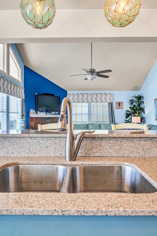 kitchen with light stone counters, vaulted ceiling, ceiling fan, and sink