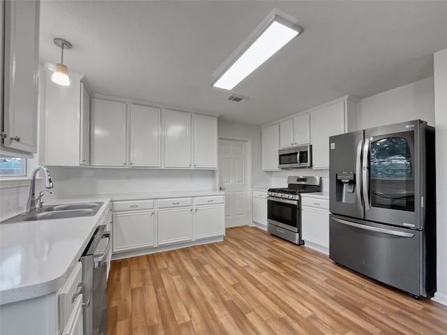 kitchen featuring white cabinets, decorative light fixtures, stainless steel appliances, and light hardwood / wood-style flooring