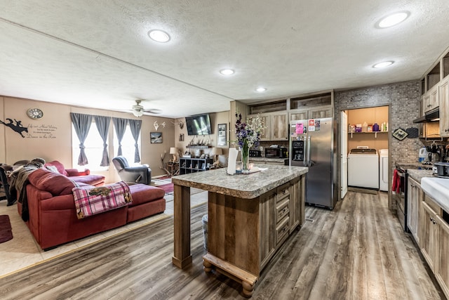 kitchen with a center island, ceiling fan, washing machine and clothes dryer, wood-type flooring, and appliances with stainless steel finishes