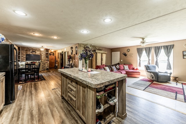 kitchen with a kitchen island, black refrigerator, ceiling fan, a textured ceiling, and hardwood / wood-style flooring