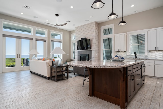 kitchen with decorative light fixtures, ceiling fan, a fireplace, white cabinets, and tasteful backsplash