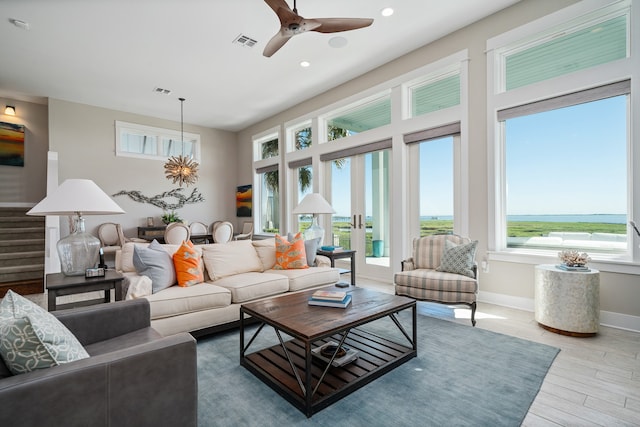 living room with a water view, ceiling fan with notable chandelier, a healthy amount of sunlight, and hardwood / wood-style flooring