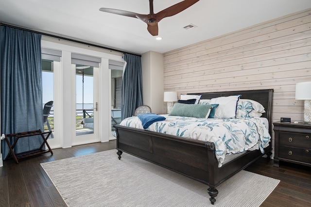 bedroom with wood walls, ceiling fan, dark hardwood / wood-style floors, and access to exterior