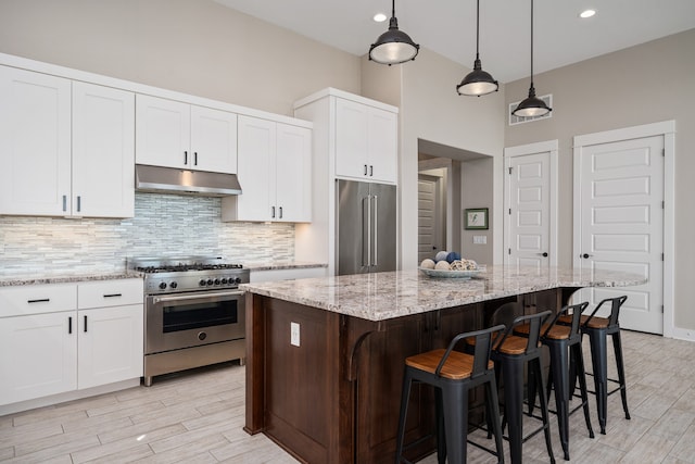 kitchen with decorative light fixtures, a kitchen island, high end appliances, white cabinetry, and backsplash