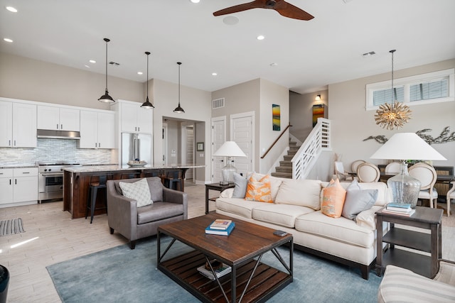 living room featuring ceiling fan with notable chandelier and light hardwood / wood-style flooring