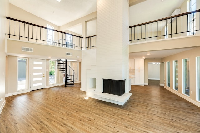 unfurnished living room featuring a brick fireplace, high vaulted ceiling, and light wood-type flooring