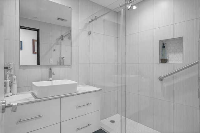 bathroom with tile walls, a shower with shower door, and vanity