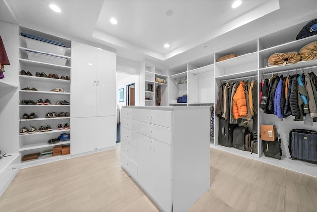 spacious closet featuring a tray ceiling and light wood-type flooring