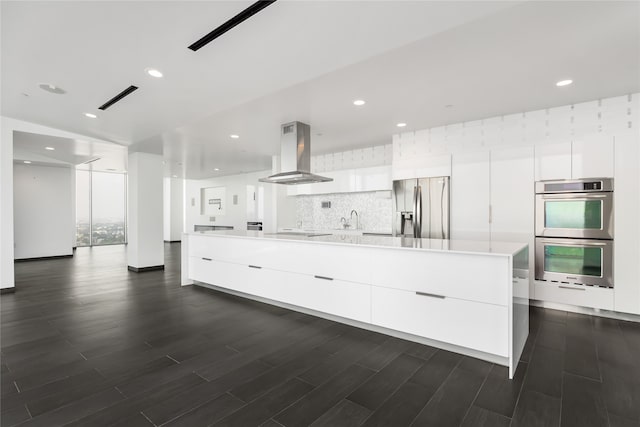 kitchen with island range hood, backsplash, white cabinetry, and appliances with stainless steel finishes