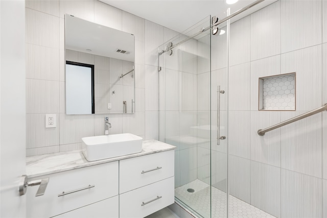 bathroom featuring tile walls, a shower with shower door, and vanity with extensive cabinet space