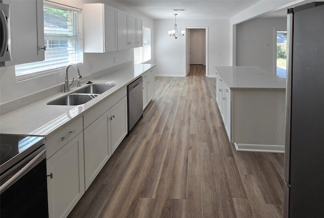 kitchen featuring hardwood / wood-style floors, appliances with stainless steel finishes, white cabinetry, sink, and pendant lighting