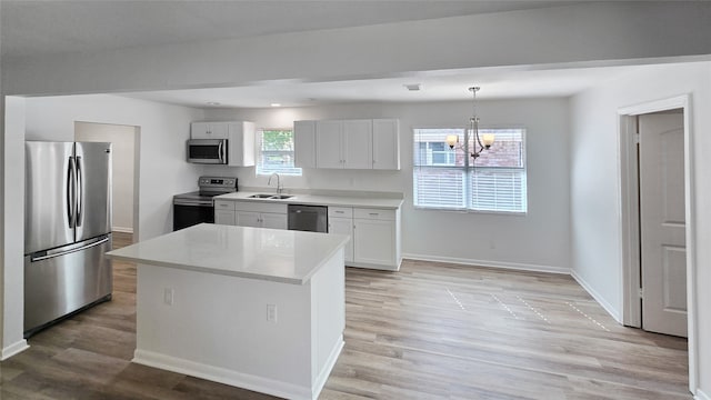 kitchen with a kitchen island, a notable chandelier, stainless steel appliances, sink, and white cabinets