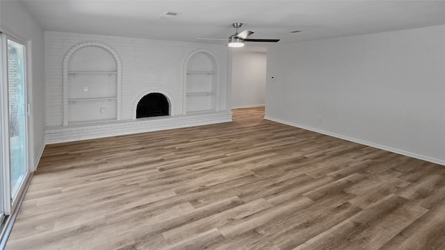 unfurnished living room featuring hardwood / wood-style flooring, a brick fireplace, built in shelves, and ceiling fan